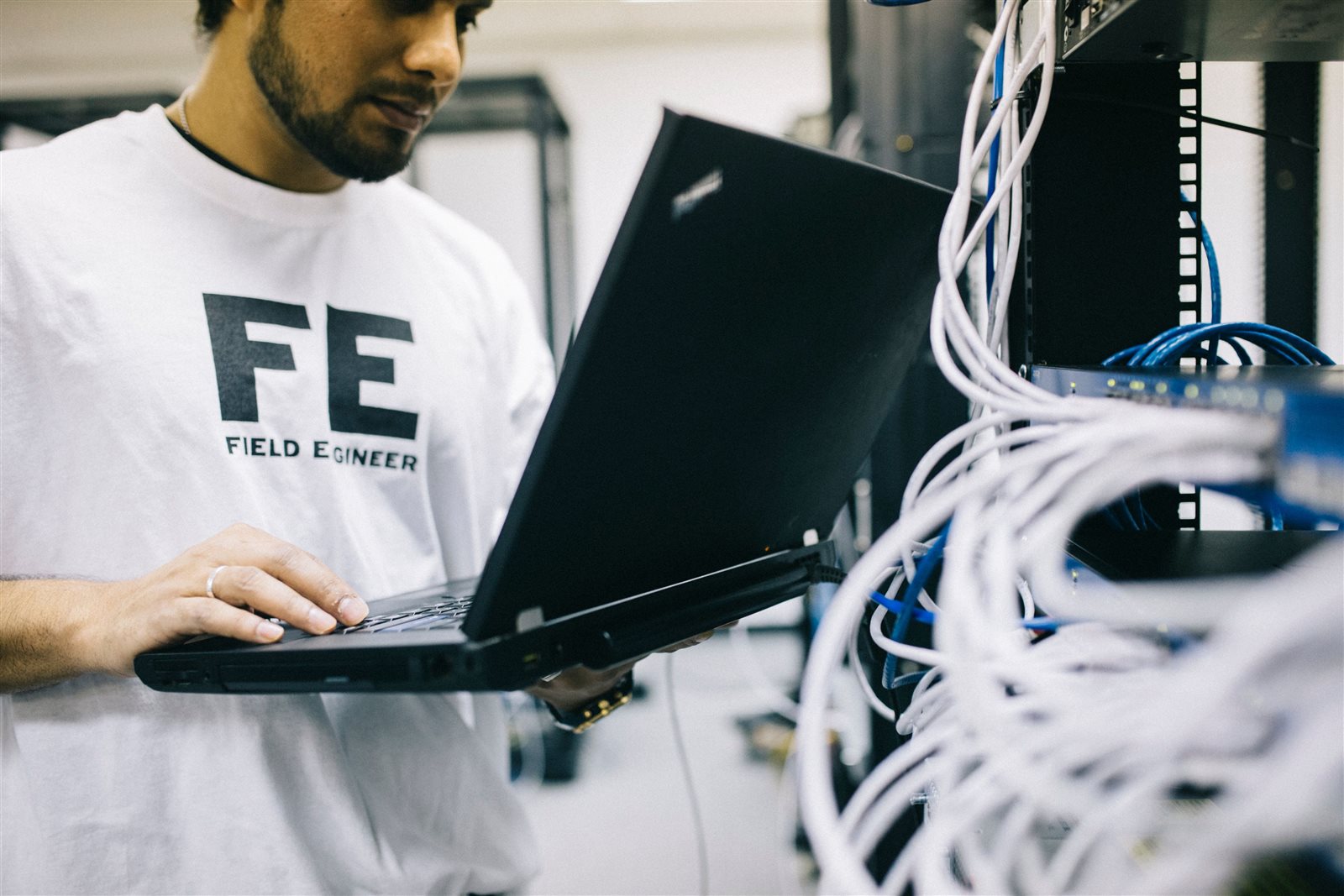 Field engineer wearing a Field Engineer t-shirt working on a laptop next to a patched server rack